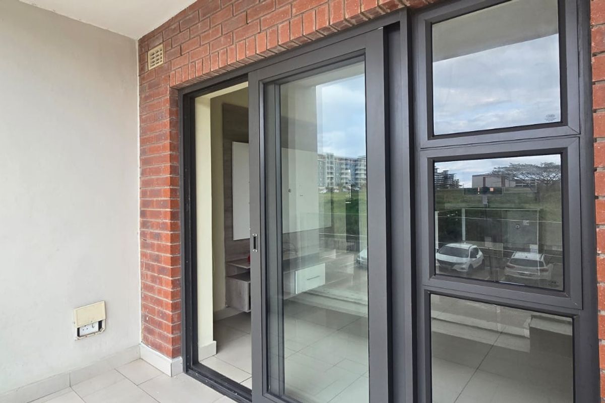 A clean, modern balcony featuring exposed brick walls, tiled flooring, and large aluminium-framed sliding glass doors providing access to the interior.