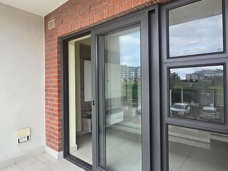 A clean, modern balcony featuring exposed brick walls, tiled flooring, and large aluminium-framed sliding glass doors providing access to the interior.
