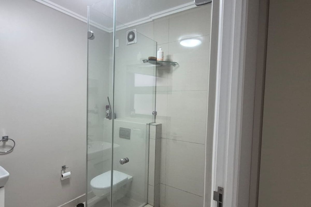 Modern bathroom featuring a wall-mounted basin, glass-enclosed shower, and wall-hung toilet with a concealed cistern, finished with neutral wall tiles.