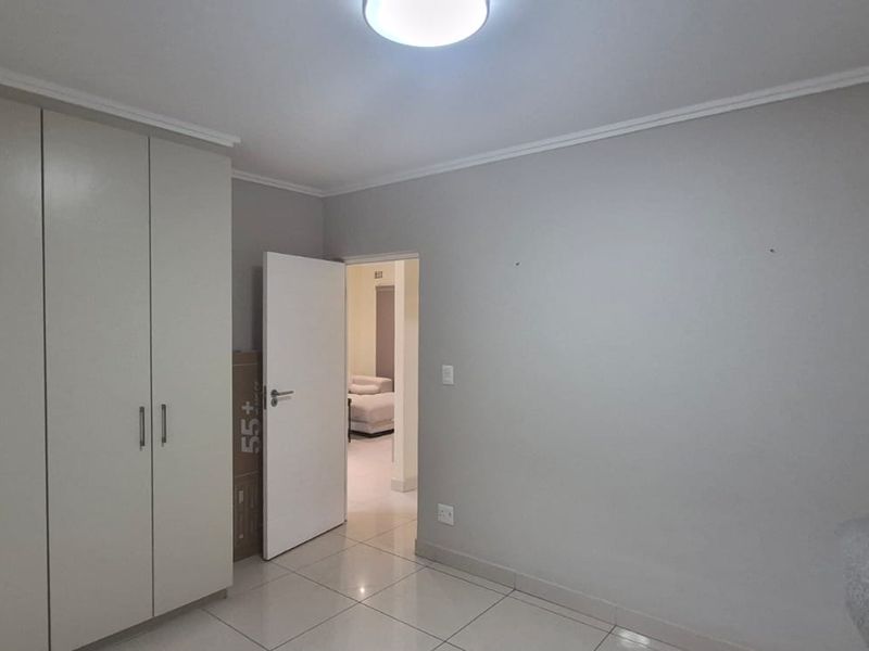 A clean, empty bedroom featuring neutral tiled flooring, built-in cupboards, and a simple ceiling light fixture.