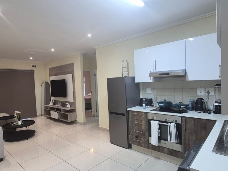 Modern open-plan living area featuring a contemporary kitchen with built-in appliances, sleek cabinetry, and bright tiled flooring throughout the combined space.