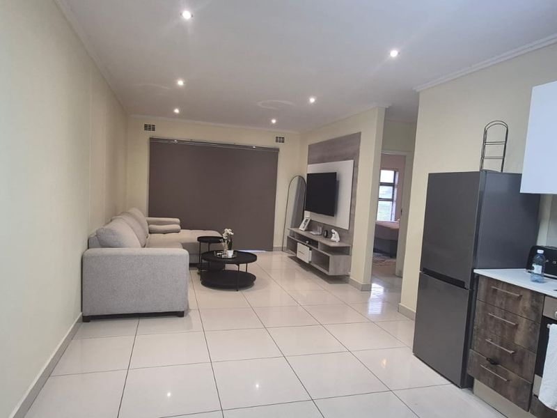 Open-plan living area featuring a modern kitchen with built-in appliances, sleek cabinetry, and tiled flooring, seamlessly flowing into the lounge space.