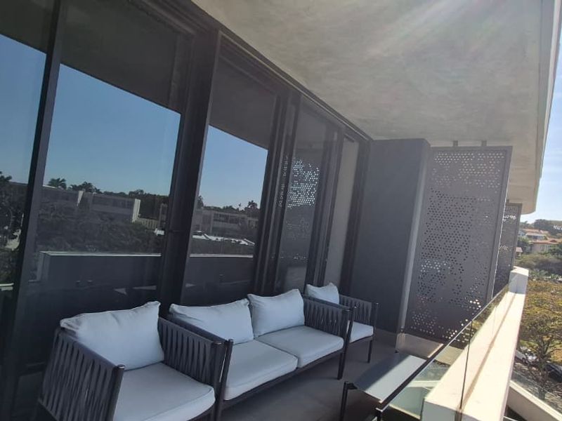 A modern balcony featuring a glass balustrade, decorative metal privacy screens, and large sliding glass doors with views of the surrounding area.