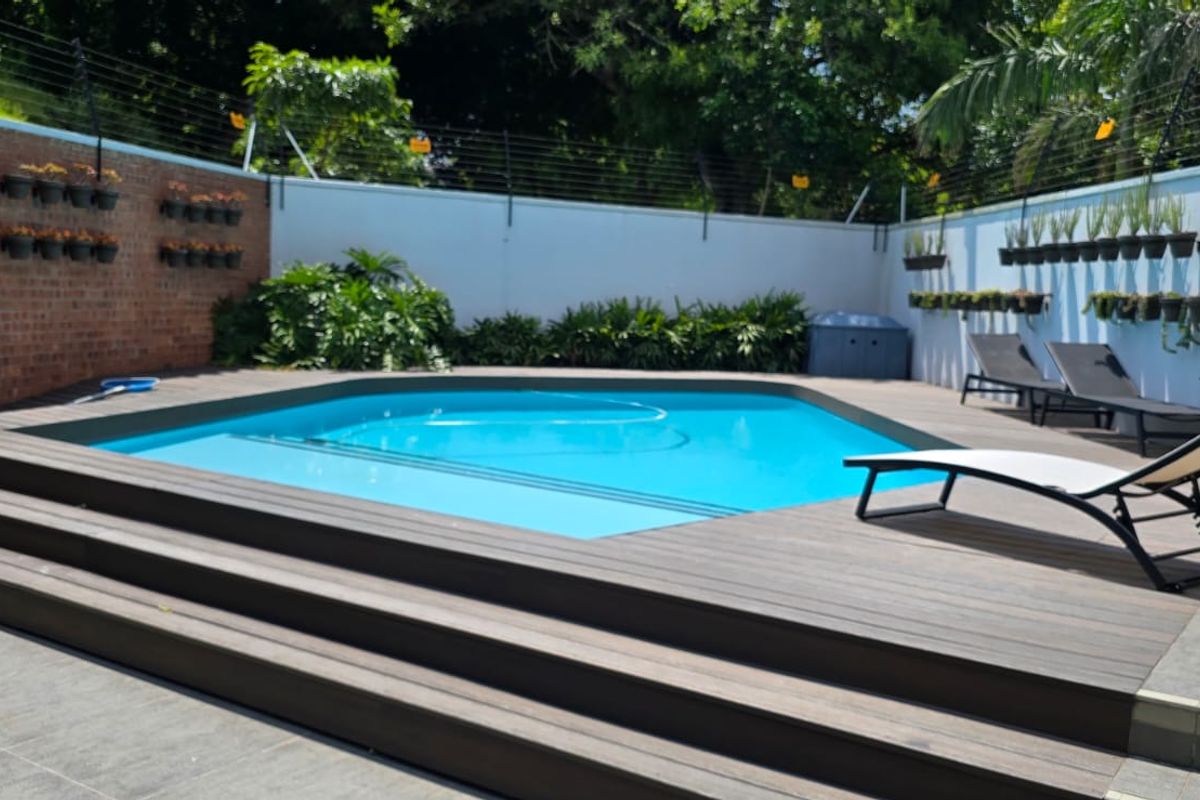 A well-maintained outdoor pool area featuring a swimming pool, raised timber decking, and secure perimeter walls with electric fencing.
