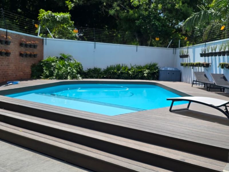 A well-maintained outdoor pool area featuring a swimming pool, raised timber decking, and secure perimeter walls with electric fencing.