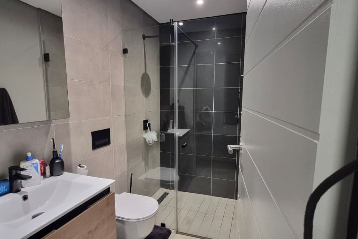 Modern bathroom featuring a vanity cabinet, wall-mounted mirror, toilet, and a walk-in shower with a glass screen and dark tiled accents.