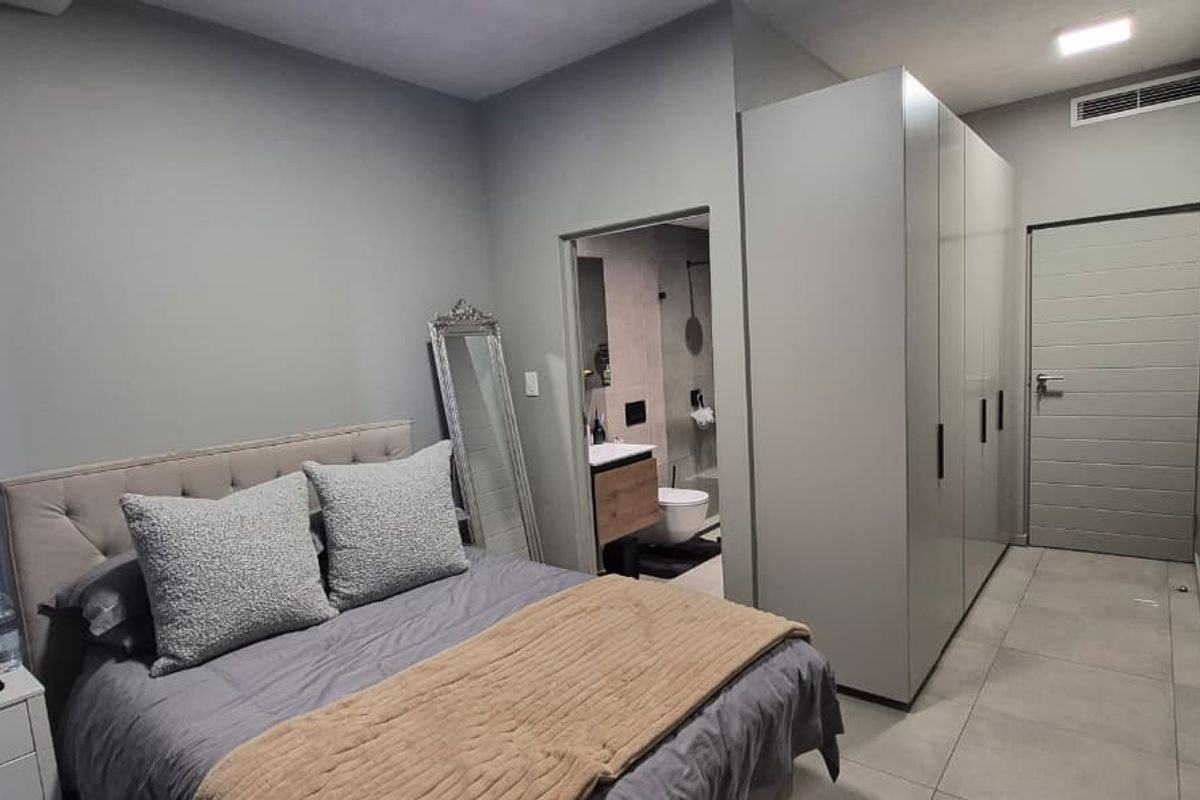 Modern bedroom featuring neutral tones, sleek built-in cupboards, tiled flooring, and direct access to an en-suite bathroom.