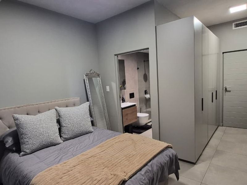 Modern bedroom featuring neutral tones, sleek built-in cupboards, tiled flooring, and direct access to an en-suite bathroom.