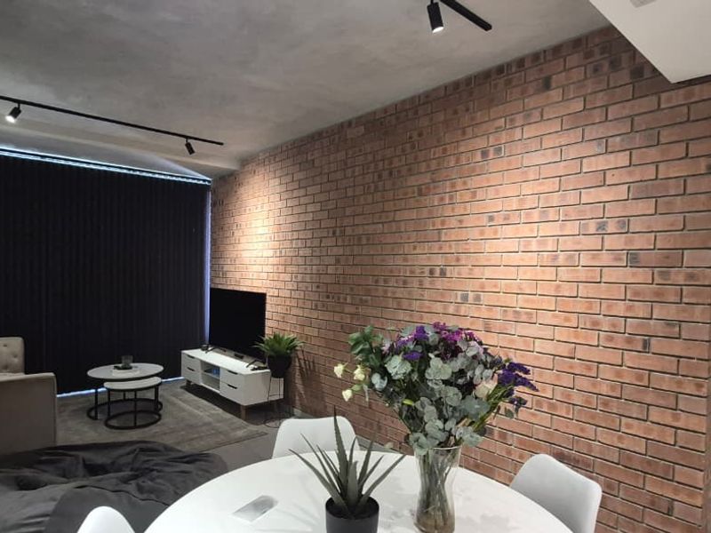 Modern open-plan living area featuring an industrial-style exposed brick feature wall, contemporary track lighting, and integrated ducted air conditioning.