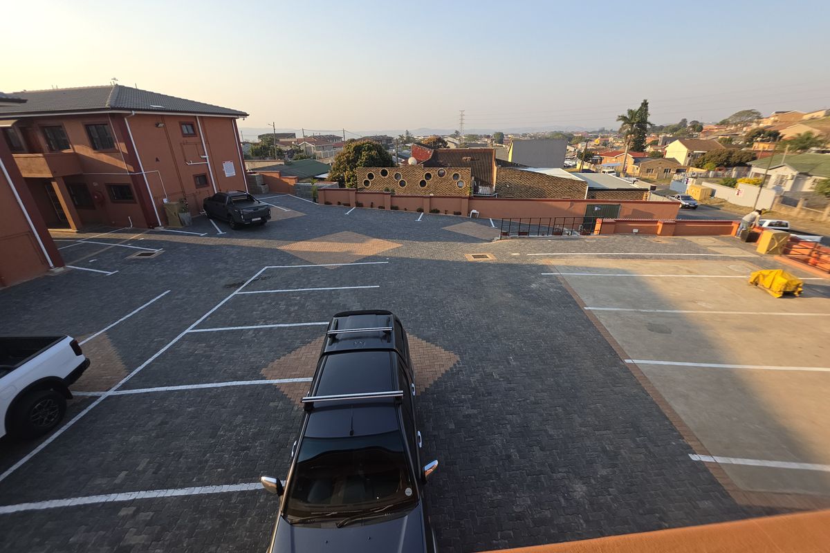 An elevated view of the apartment complex parking area featuring paved surfaces and perimeter boundary walls.