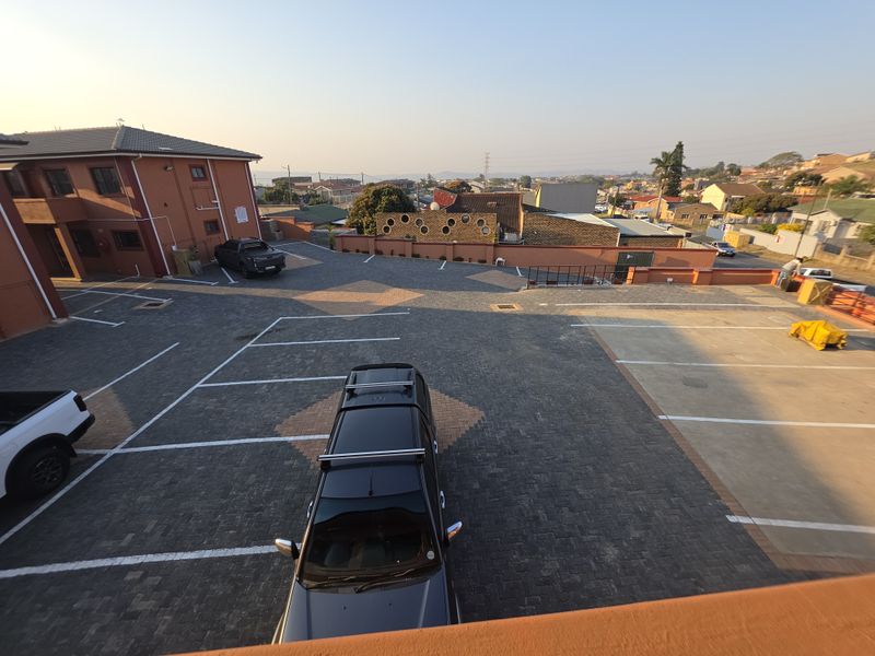 An elevated view of the apartment complex parking area featuring paved surfaces and perimeter boundary walls.