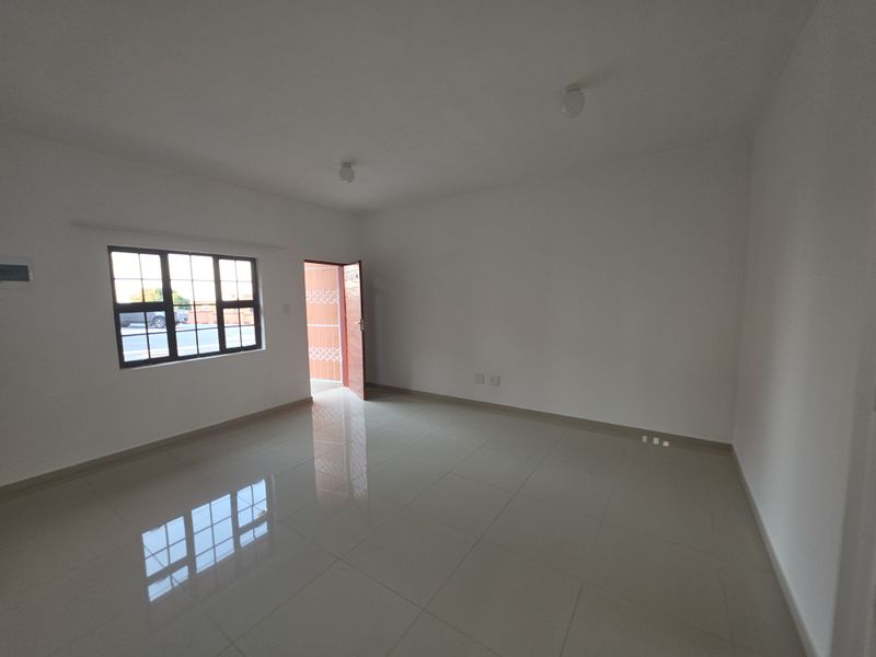 A bright, empty living area featuring polished tiled flooring, neutral walls, and a grid-pattern window providing natural light.