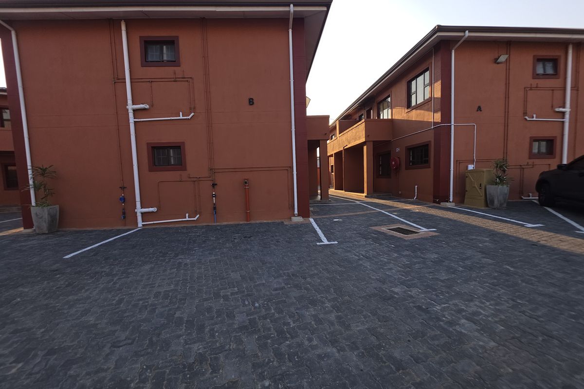 Exterior view of the apartment complex showing the paved parking area between two residential blocks with painted masonry facades.