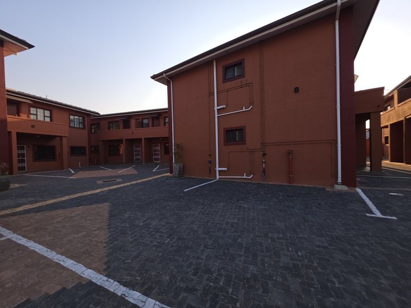 Exterior view of the apartment complex featuring paved parking areas and multi-story residential blocks with external plumbing and security access points.