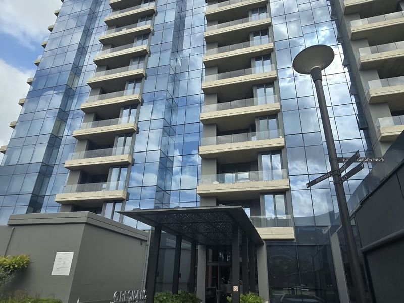 Modern high-rise apartment building featuring a glass facade, multiple balconies, and a covered entrance canopy.