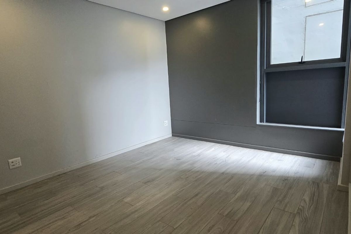 A clean, empty bedroom featuring modern laminate flooring, a dark accent wall, and a large window providing natural light.