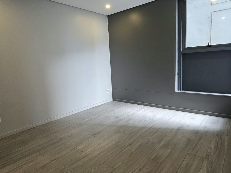 A clean, empty bedroom featuring modern laminate flooring, a dark accent wall, and a large window providing natural light.