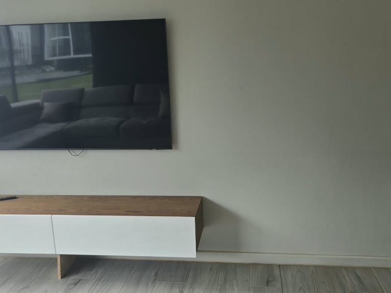 A modern living area featuring light-toned tiled flooring and a sleek, wall-mounted media console unit.