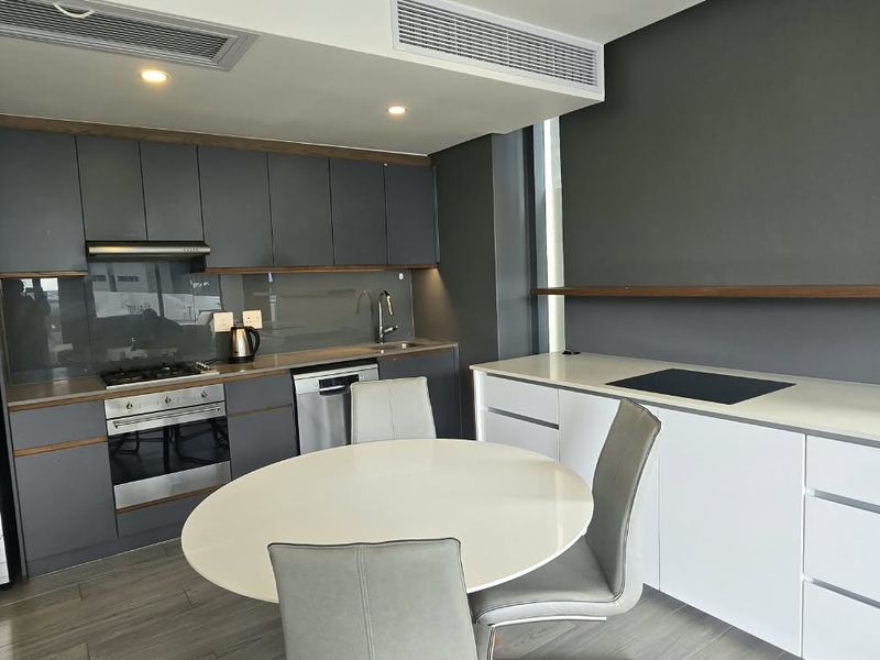 Modern open-plan kitchen featuring sleek grey cabinetry, stone countertops, integrated appliances, and ducted air conditioning in a contemporary apartment setting.