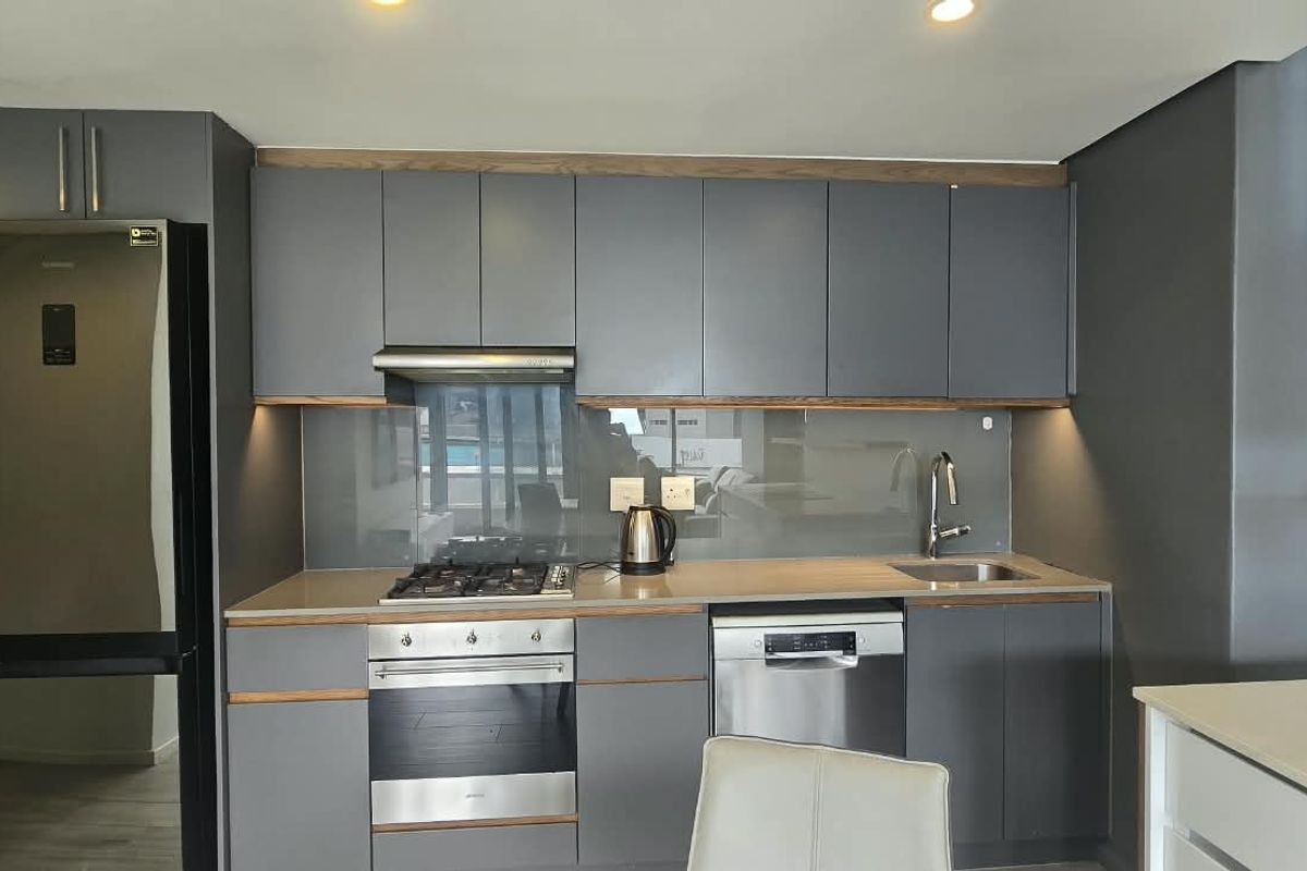 Modern kitchen featuring dark grey cabinetry, stone countertops, glass splashback, and integrated appliances including a gas hob, oven, and dishwasher.