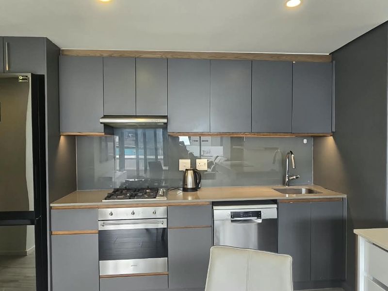Modern kitchen featuring dark grey cabinetry, stone countertops, glass splashback, and integrated appliances including a gas hob, oven, and dishwasher.