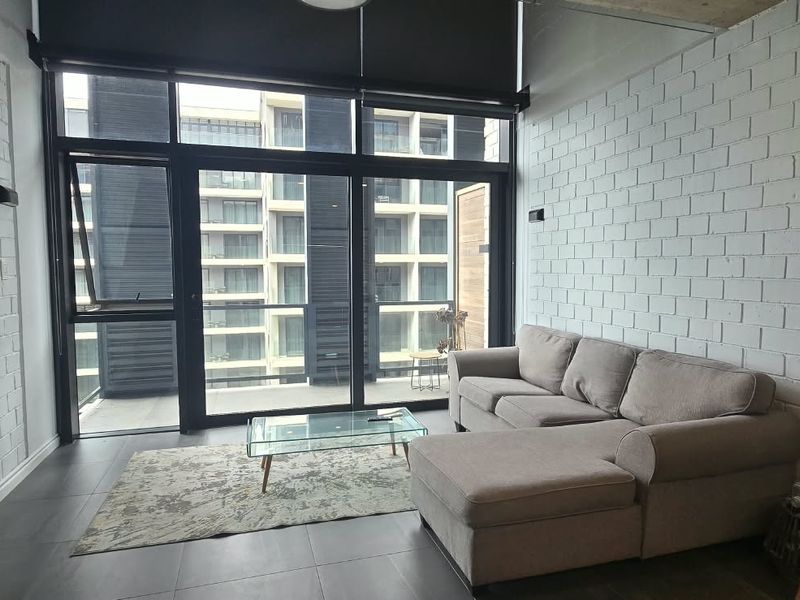 Modern living room featuring exposed white brick walls, large floor-to-ceiling windows with roller blinds, and tiled flooring, providing access to a balcony.