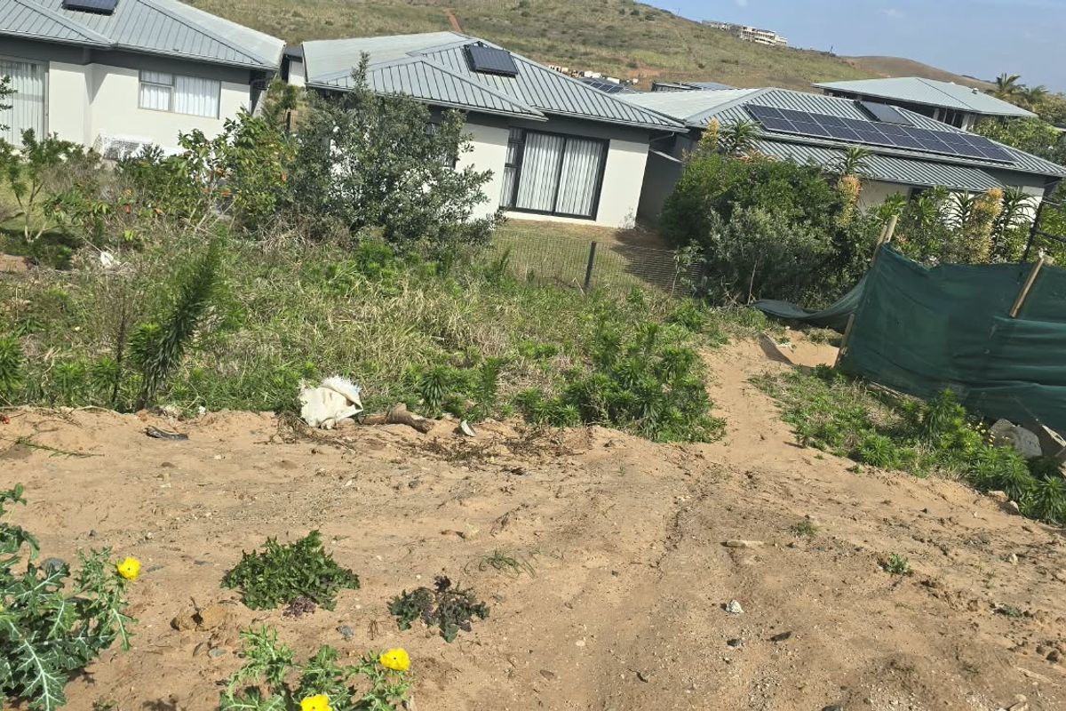 A sloped residential plot showing natural terrain, perimeter fencing, and surrounding established homes in a residential estate setting.