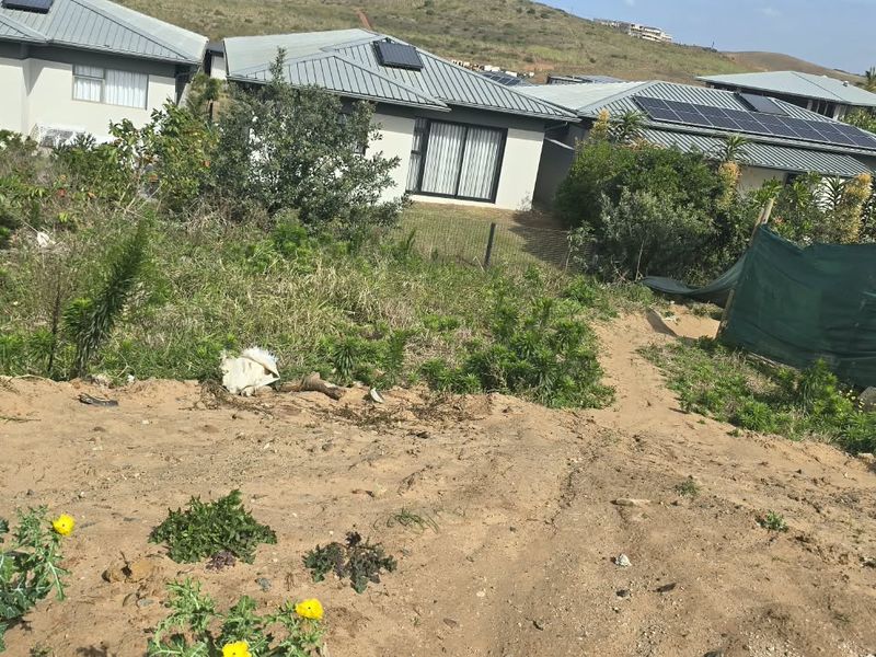 A sloped residential plot showing natural terrain, perimeter fencing, and surrounding established homes in a residential estate setting.