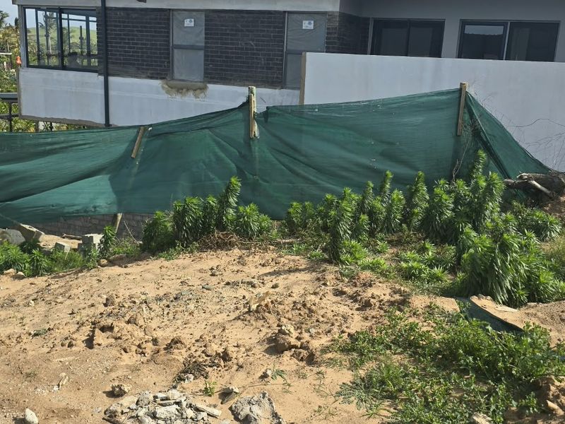 A view of a vacant residential plot showing unimproved soil, construction debris, and temporary site fencing adjacent to a neighboring property.