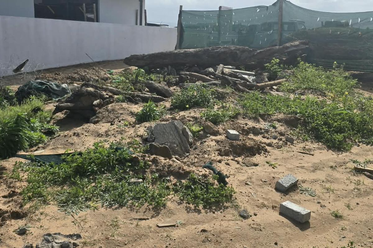 An undeveloped residential plot featuring uneven sandy terrain, scattered debris, and perimeter boundary walls.