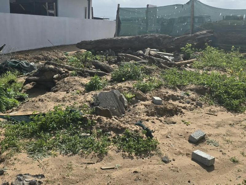 An undeveloped residential plot featuring uneven sandy terrain, scattered debris, and perimeter boundary walls.