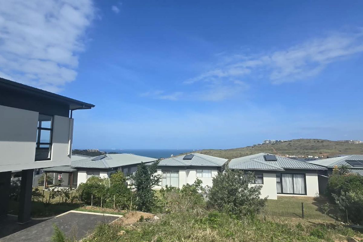 An elevated view overlooking a residential estate with modern homes, featuring metal roofs with integrated solar panels and distant coastal scenery.