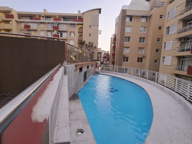 Communal swimming pool area situated between apartment blocks, featuring paved decking and metal safety balustrades.