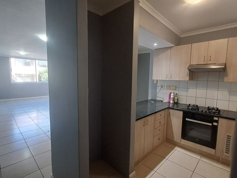 Open-plan apartment layout featuring a functional kitchen with built-in cabinetry, granite countertops, and integrated appliances, flowing into a spacious, tiled living area.
