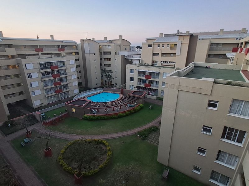 An elevated aerial view of the apartment complex courtyard, featuring a central swimming pool, landscaped garden areas, and paved walkways between residential blocks.