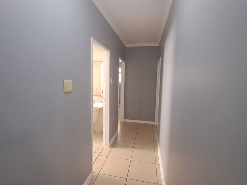 A clean, neutral-toned hallway featuring tiled flooring and access to adjacent rooms, providing a simple and functional transition space within the apartment.