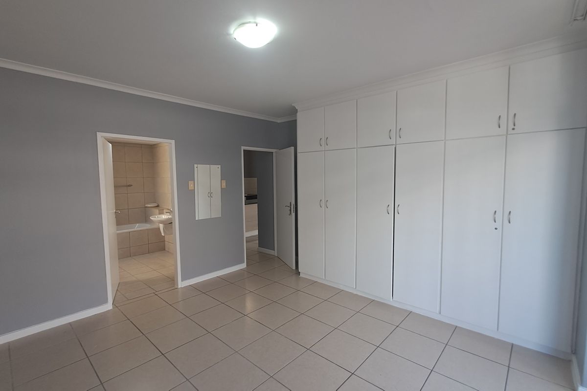 Spacious bedroom featuring neutral grey walls, tiled flooring, and extensive built-in white cabinetry, with direct access to an en-suite bathroom.