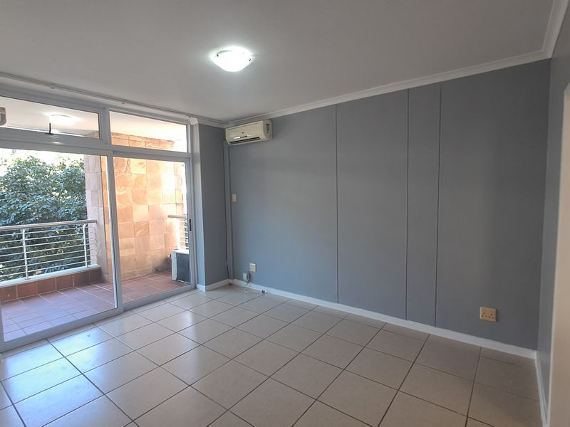 A bright, empty living room featuring tiled floors, a wall-mounted air conditioning unit, and large sliding glass doors leading to a private balcony.