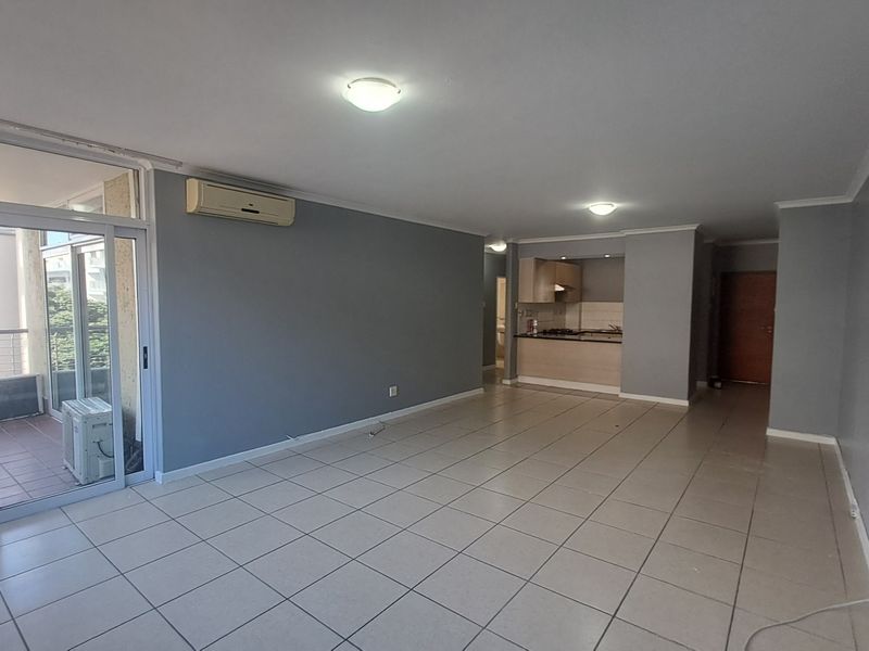Spacious open-plan living area featuring tiled flooring, an air conditioning unit, and direct access to a balcony, with an adjoining kitchen space.