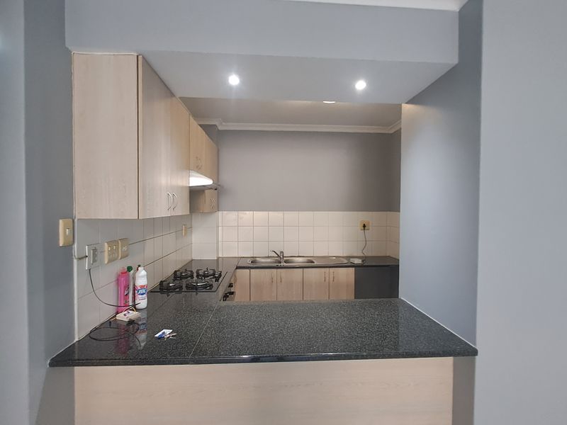 A functional kitchen featuring light wood cabinetry, dark granite countertops, a gas hob, and a tiled backsplash with a convenient breakfast bar.