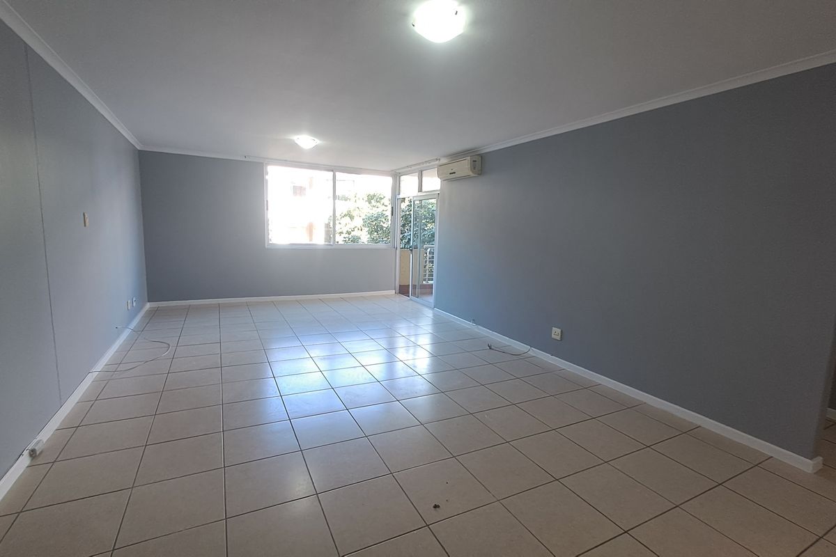 A spacious, empty living area featuring neutral grey walls, tiled flooring, and an integrated air conditioning unit with access to an outdoor balcony.