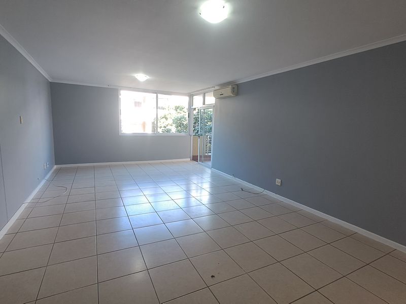 A spacious, empty living area featuring neutral grey walls, tiled flooring, and an integrated air conditioning unit with access to an outdoor balcony.