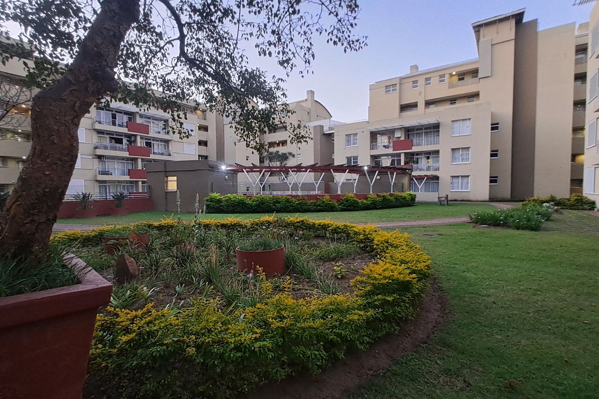A view of the communal garden and courtyard area between apartment blocks, featuring landscaped beds and paved pathways.