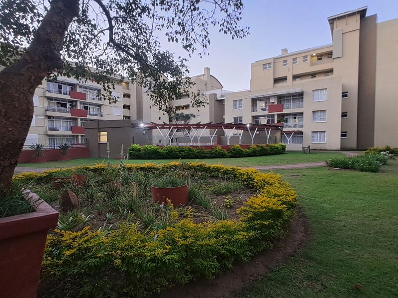 A view of the communal garden and courtyard area between apartment blocks, featuring landscaped beds and paved pathways.