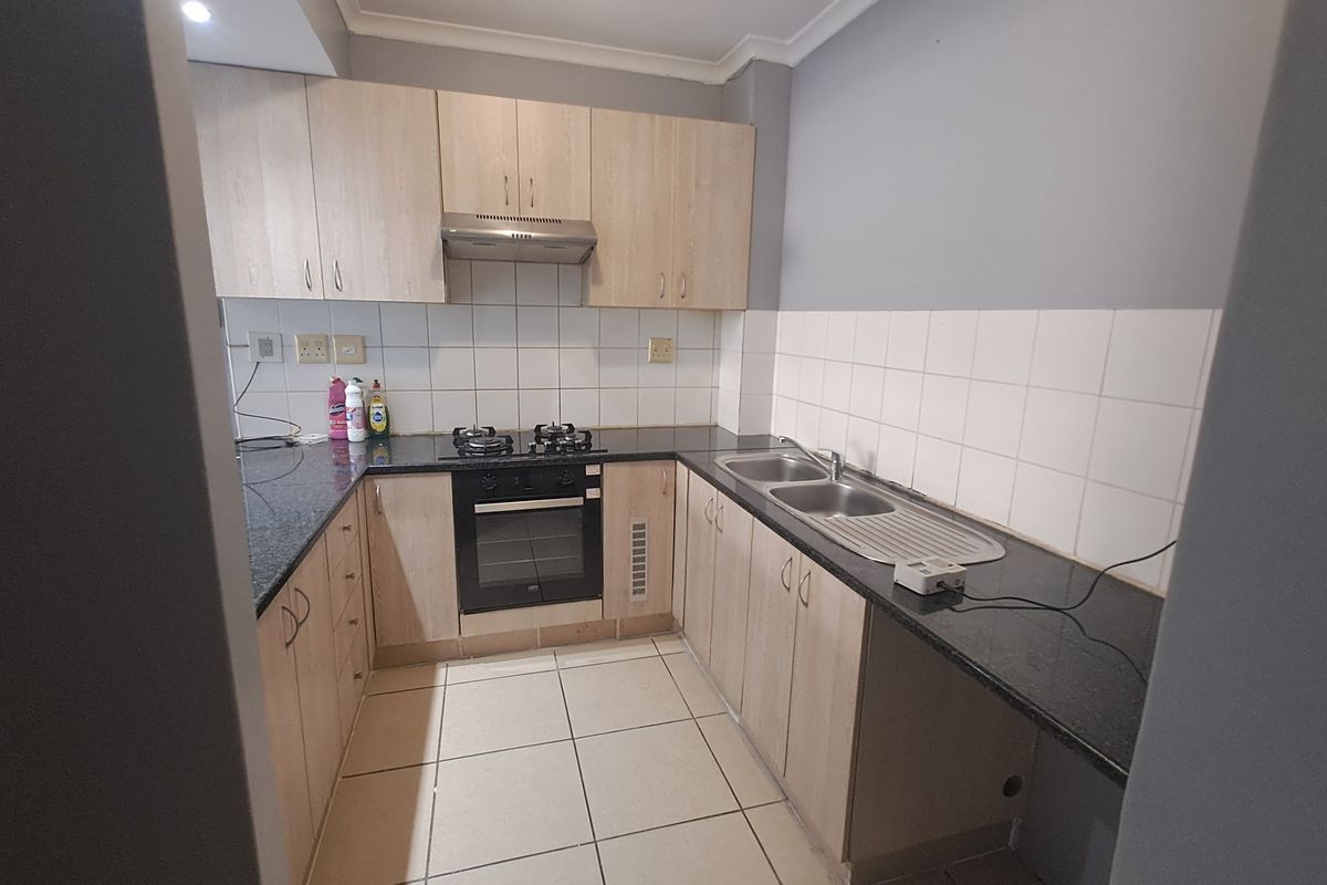 A functional kitchen featuring light wood cabinetry, granite countertops, a gas hob, built-in oven, and a double sink with tiled backsplash.