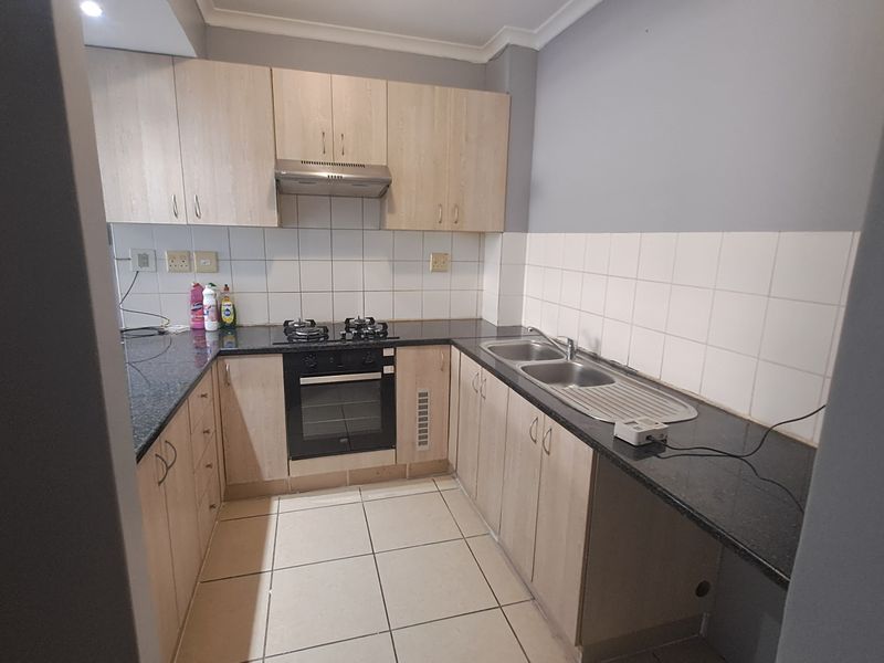 A functional kitchen featuring light wood cabinetry, granite countertops, a gas hob, built-in oven, and a double sink with tiled backsplash.
