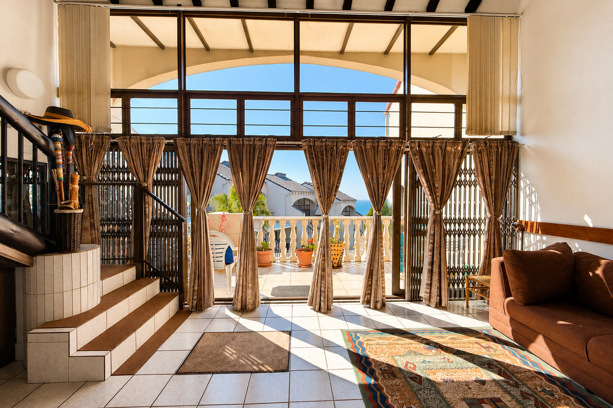 Spacious living area featuring tiled floors, exposed timber beams, and large glass doors opening onto a balcony with scenic views.