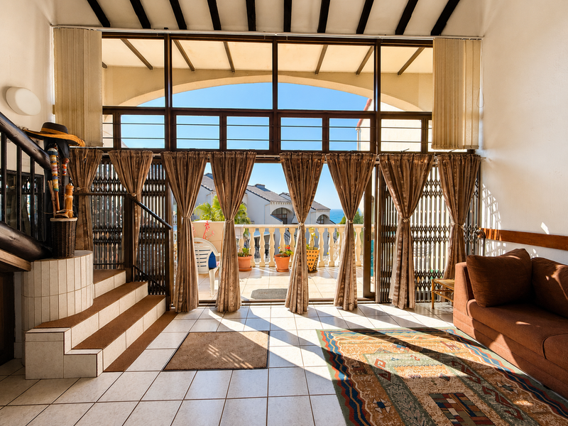 Spacious living area featuring tiled floors, exposed timber beams, and large glass doors opening onto a balcony with scenic views.