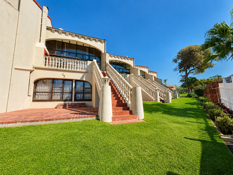 Rear view of the apartment complex featuring a landscaped lawn, brick patio area, and external staircases leading to upper-level balconies.