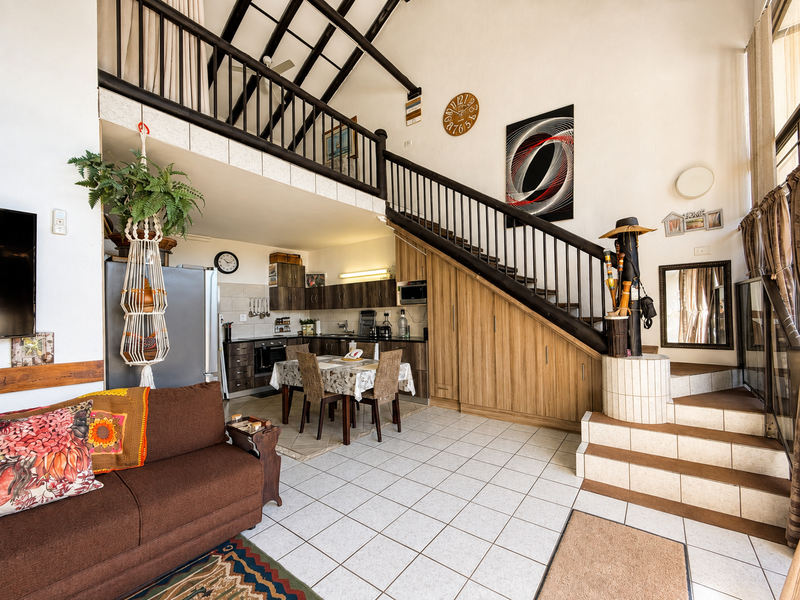 Open-plan living area featuring a kitchen with built-in cabinetry, a staircase leading to a mezzanine level, and tiled flooring throughout.